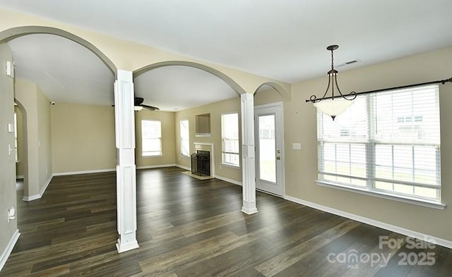 unfurnished dining area featuring baseboards, arched walkways, dark wood-style flooring, and a fireplace
