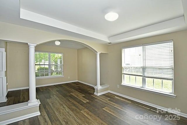 unfurnished living room with ornate columns, wood finished floors, arched walkways, and baseboards