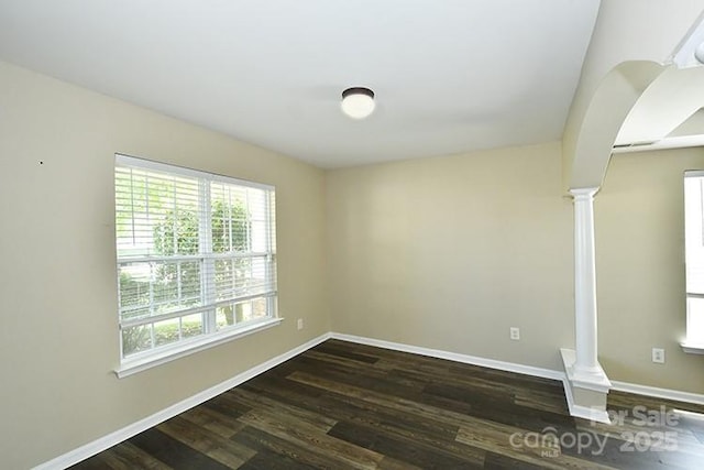 spare room featuring a healthy amount of sunlight, dark wood-type flooring, and ornate columns