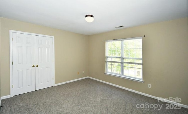 unfurnished bedroom with a closet, dark colored carpet, and baseboards