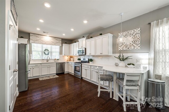 kitchen with dark wood-style flooring, a sink, stainless steel appliances, white cabinetry, and backsplash