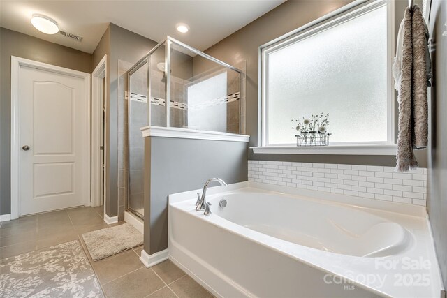 bathroom featuring tile patterned flooring, visible vents, baseboards, a bath, and a stall shower