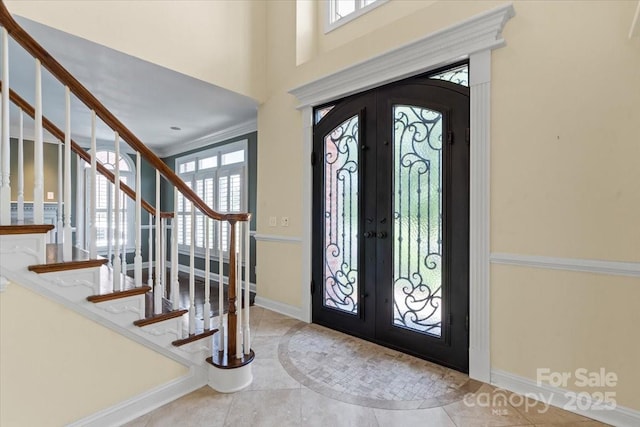 tiled entrance foyer featuring french doors, stairway, baseboards, arched walkways, and ornamental molding