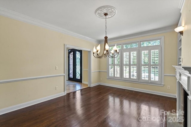 unfurnished dining area featuring a chandelier, dark wood finished floors, baseboards, crown molding, and a fireplace