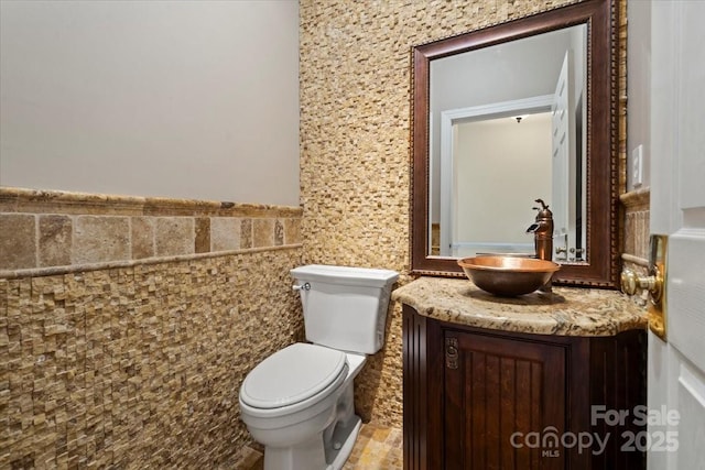 bathroom featuring toilet, vanity, wainscoting, and tile walls