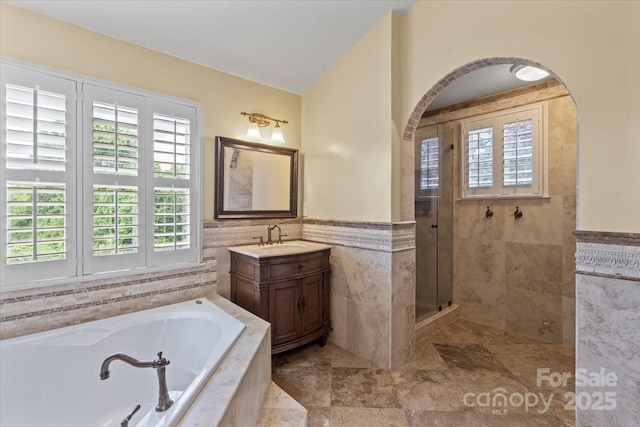 full bathroom with tile walls, healthy amount of natural light, tiled shower, a bath, and vanity