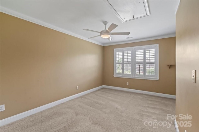 carpeted empty room with attic access, crown molding, baseboards, and ceiling fan