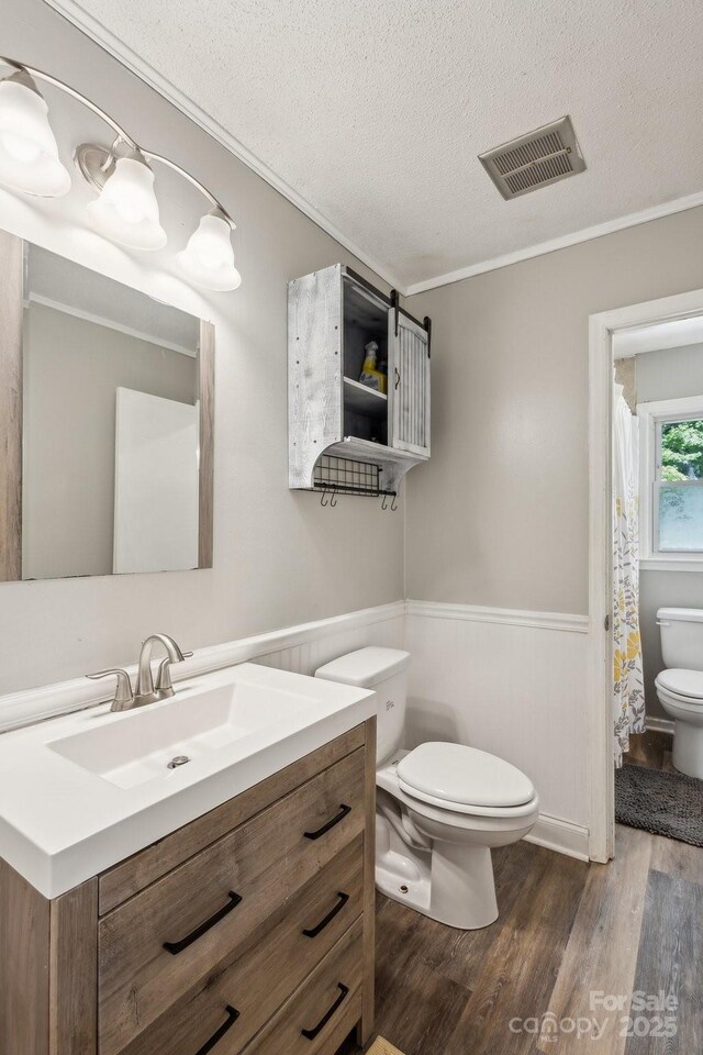 6412 Old Meadow Rd, Charlotte, NC 28227 - full bath featuring toilet, wood finished floors, a textured ceiling, a wainscoted wall, and ornamental molding