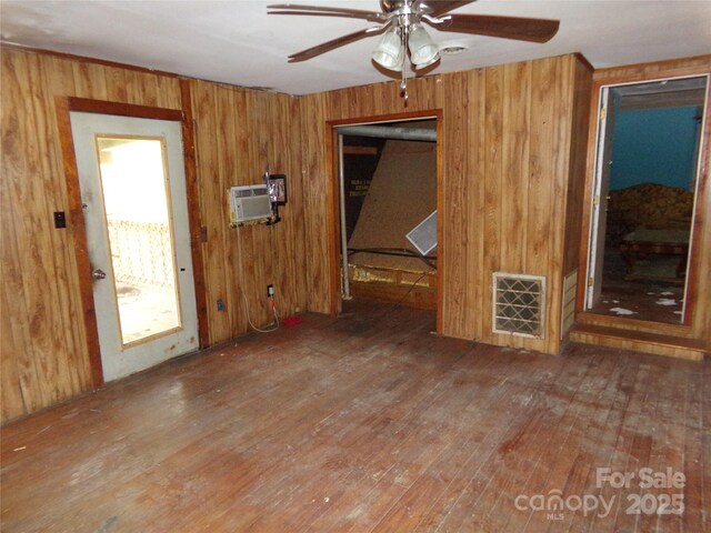 unfurnished living room with wooden walls, visible vents, a ceiling fan, wood-type flooring, and a wall mounted AC