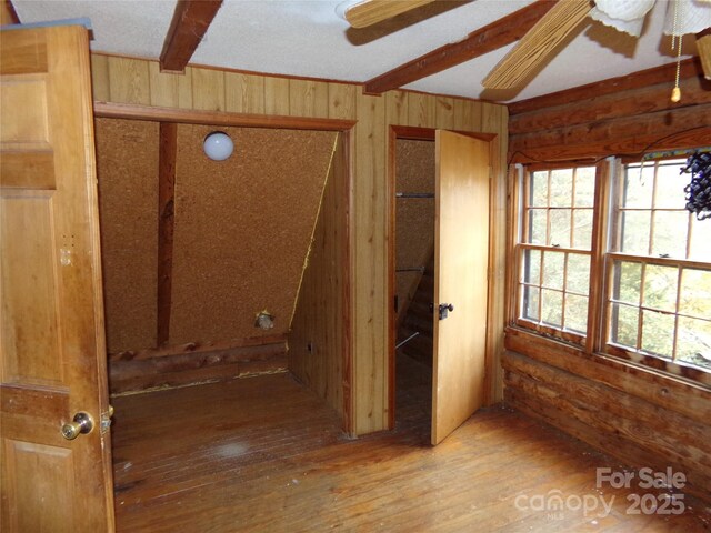 empty room featuring ceiling fan, wood walls, beam ceiling, and hardwood / wood-style floors