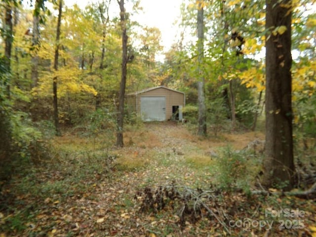 view of yard featuring an outdoor structure, dirt driveway, a wooded view, and a garage