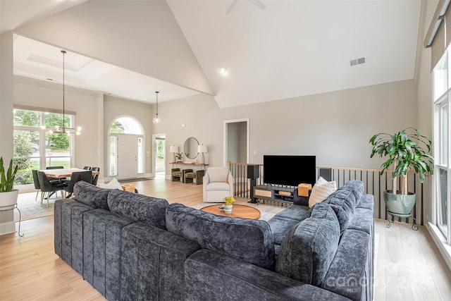 living area featuring an inviting chandelier, high vaulted ceiling, light wood finished floors, and visible vents
