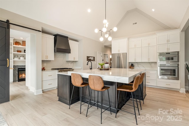 kitchen featuring a glass covered fireplace, custom exhaust hood, light countertops, white cabinets, and stainless steel appliances