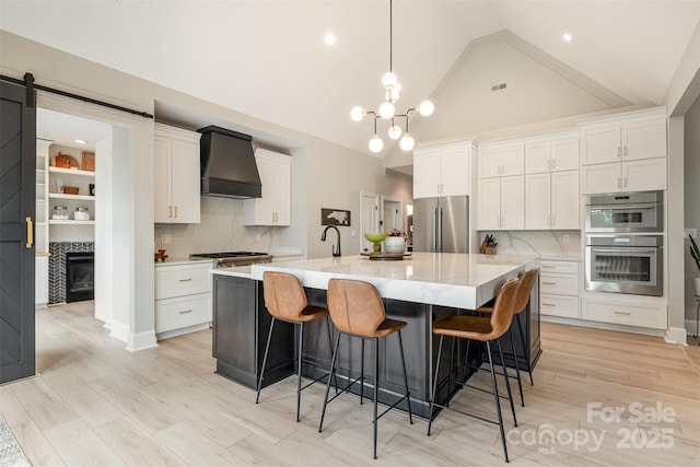 kitchen with tasteful backsplash, a large island with sink, custom range hood, stainless steel appliances, and white cabinetry