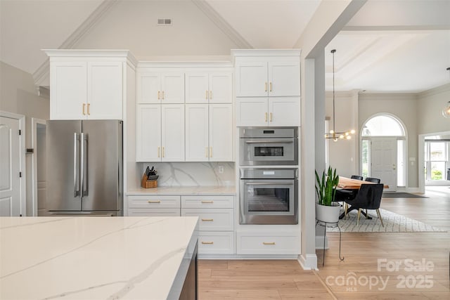 kitchen featuring an inviting chandelier, light wood-style floors, white cabinets, light stone counters, and appliances with stainless steel finishes