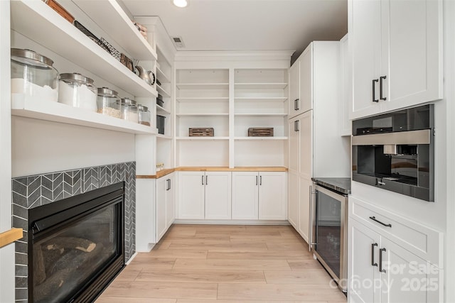 interior space with open shelves, light wood-style floors, black oven, white cabinetry, and wine cooler