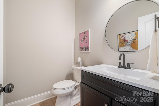 half bath featuring vanity, baseboards, wood finished floors, and toilet