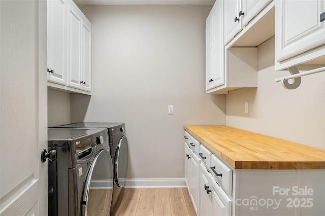laundry area featuring separate washer and dryer, cabinet space, baseboards, and light wood-type flooring