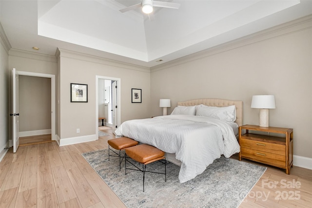 bedroom featuring a raised ceiling, baseboards, ornamental molding, and light wood-style flooring