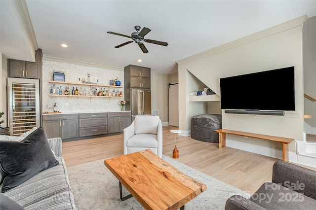 living room with ceiling fan, a dry bar, light wood-style flooring, wine cooler, and ornamental molding