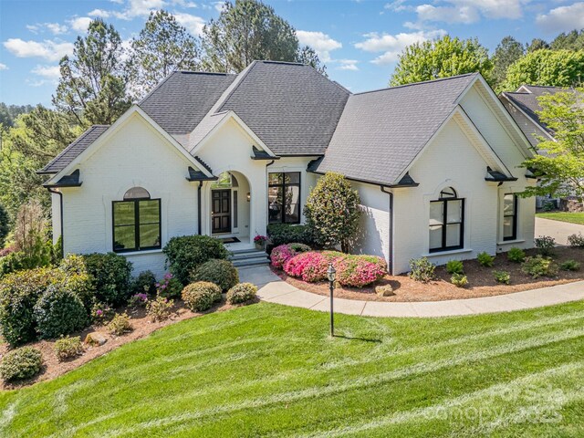 view of front of property featuring brick siding, a front lawn, and roof with shingles