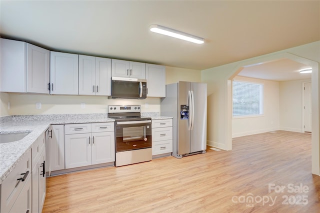 kitchen featuring arched walkways, baseboards, light stone counters, light wood-style floors, and stainless steel appliances