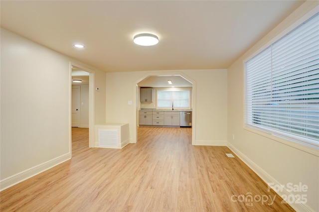 unfurnished living room with light wood-type flooring, arched walkways, baseboards, and visible vents