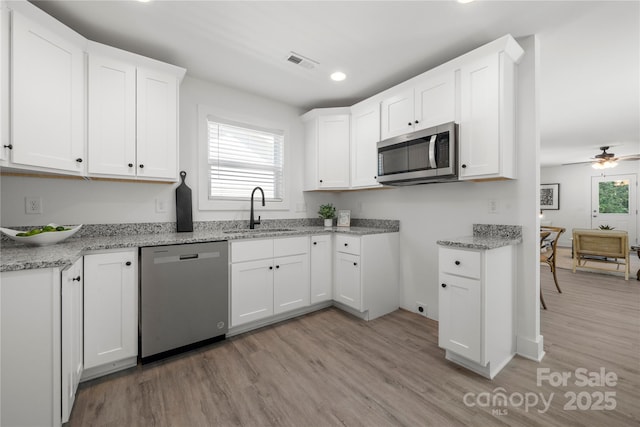 3205 Morning Dr, Charlotte, NC 28208 - kitchen with visible vents, white cabinets, a sink, light wood finished floors, and appliances with stainless steel finishes