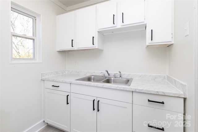 kitchen with a sink, light countertops, white cabinets, and baseboards