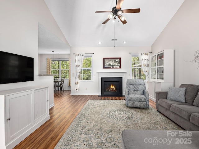 living area featuring lofted ceiling, wood finished floors, a ceiling fan, and a fireplace with flush hearth