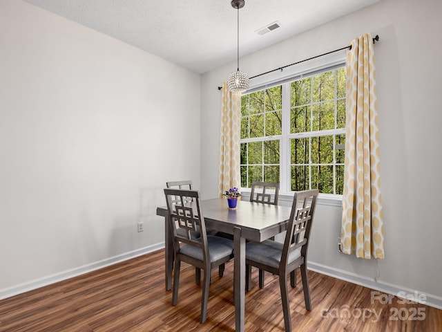 dining space featuring a textured ceiling, visible vents, baseboards, wood finished floors, and a notable chandelier