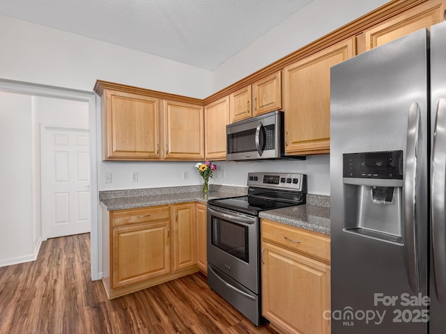 kitchen with appliances with stainless steel finishes, dark wood-type flooring, dark countertops, and light brown cabinetry