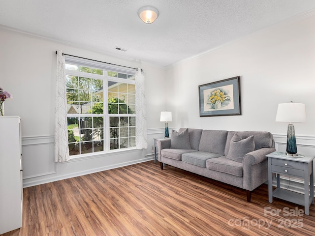 living area with visible vents, wood finished floors, a wainscoted wall, and ornamental molding