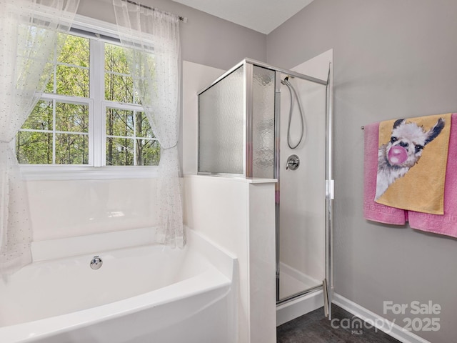 bathroom featuring a shower stall, a bath, and baseboards