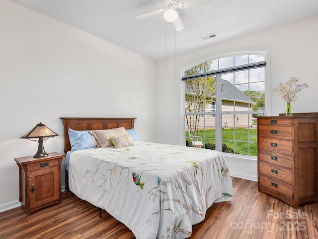 bedroom with multiple windows, baseboards, wood finished floors, and visible vents