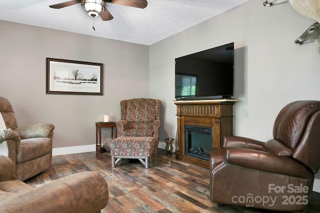 living area with a fireplace, wood-type flooring, ceiling fan, baseboards, and a textured ceiling