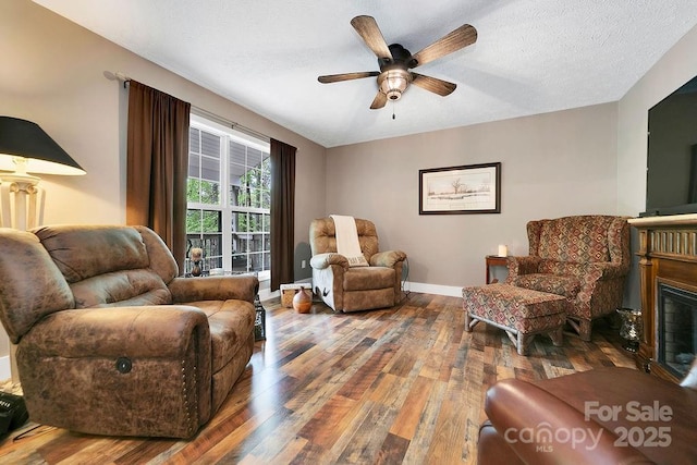 sitting room featuring wood-type flooring, a glass covered fireplace, a ceiling fan, baseboards, and a textured ceiling