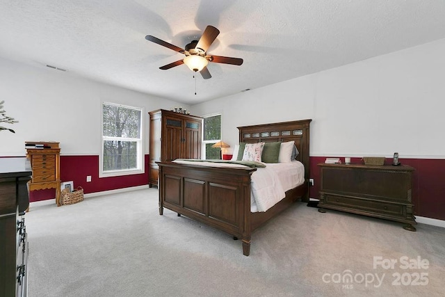 bedroom with a textured ceiling, light colored carpet, visible vents, ceiling fan, and baseboards