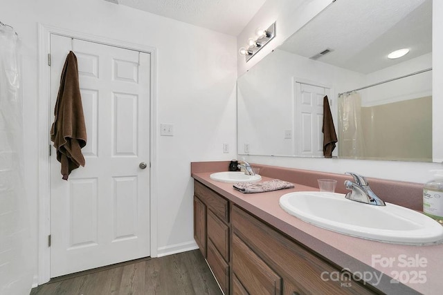full bathroom with visible vents, wood finished floors, double vanity, and a sink
