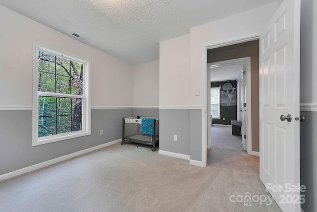 carpeted empty room featuring a textured ceiling, visible vents, and baseboards