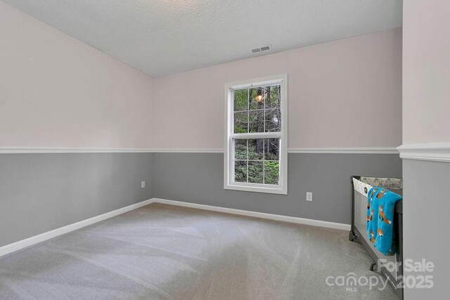 unfurnished room with a textured ceiling, visible vents, carpet flooring, and baseboards