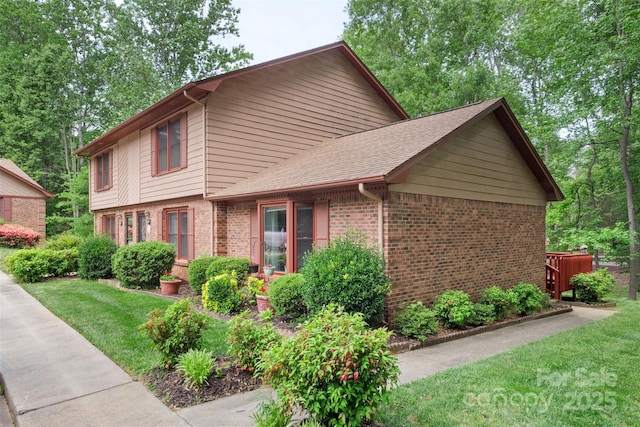 view of side of property featuring a shingled roof, a yard, and brick siding