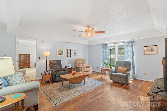 living room with wood finished floors, baseboards, a raised ceiling, a textured ceiling, and a ceiling fan