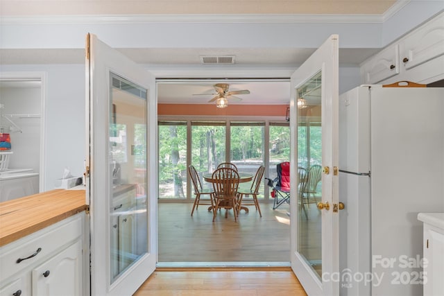 interior space with visible vents, crown molding, ceiling fan, french doors, and light wood finished floors