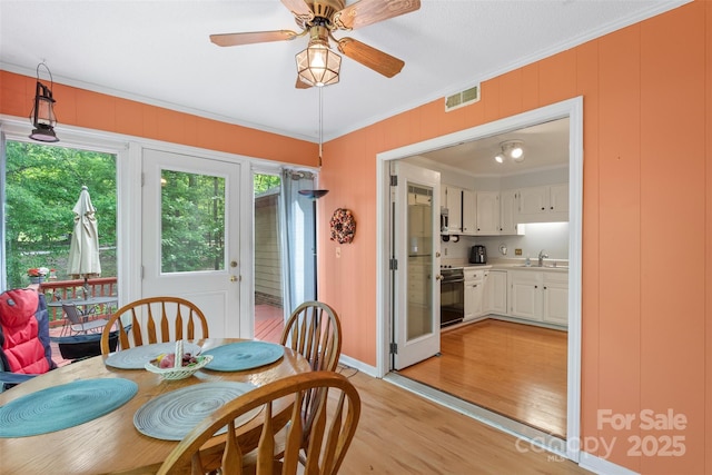 dining area featuring crown molding, light wood-style floors, a ceiling fan, baseboards, and visible vents