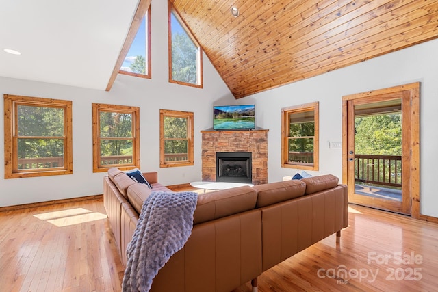 living room featuring high vaulted ceiling, light wood finished floors, a stone fireplace, and baseboards