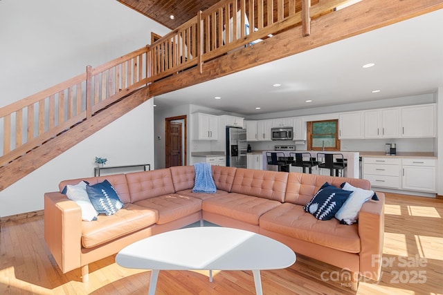 living room with light wood-type flooring, a towering ceiling, stairway, and recessed lighting