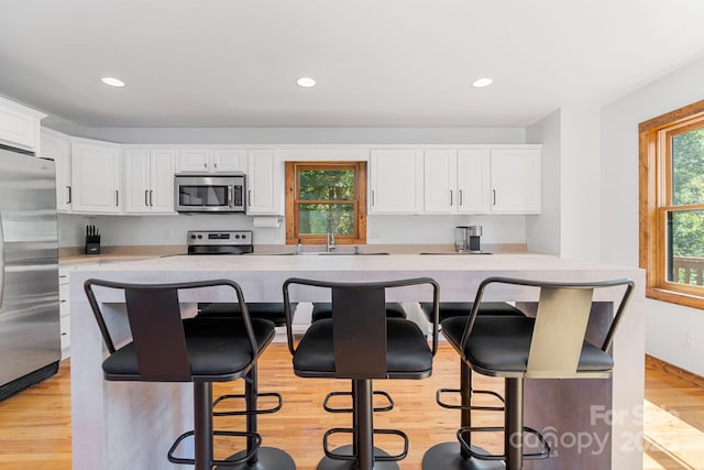 kitchen with white cabinets, a sink, appliances with stainless steel finishes, a breakfast bar, and light wood-type flooring