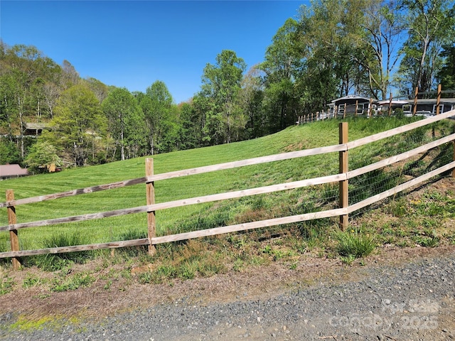 view of gate with a lawn, a view of trees, fence, and a rural view