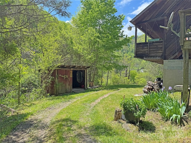 view of yard featuring a forest view, an outbuilding, and a shed